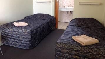 A room with two beds, each with a patterned bedspread and a folded towel. There is a door leading to a bathroom with a sink and mirror.