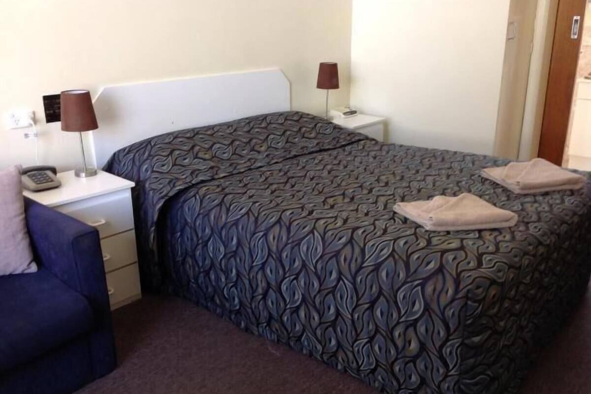 A hotel room with a bed, two bedside tables, a lamp, a chair, and a carpeted floor.