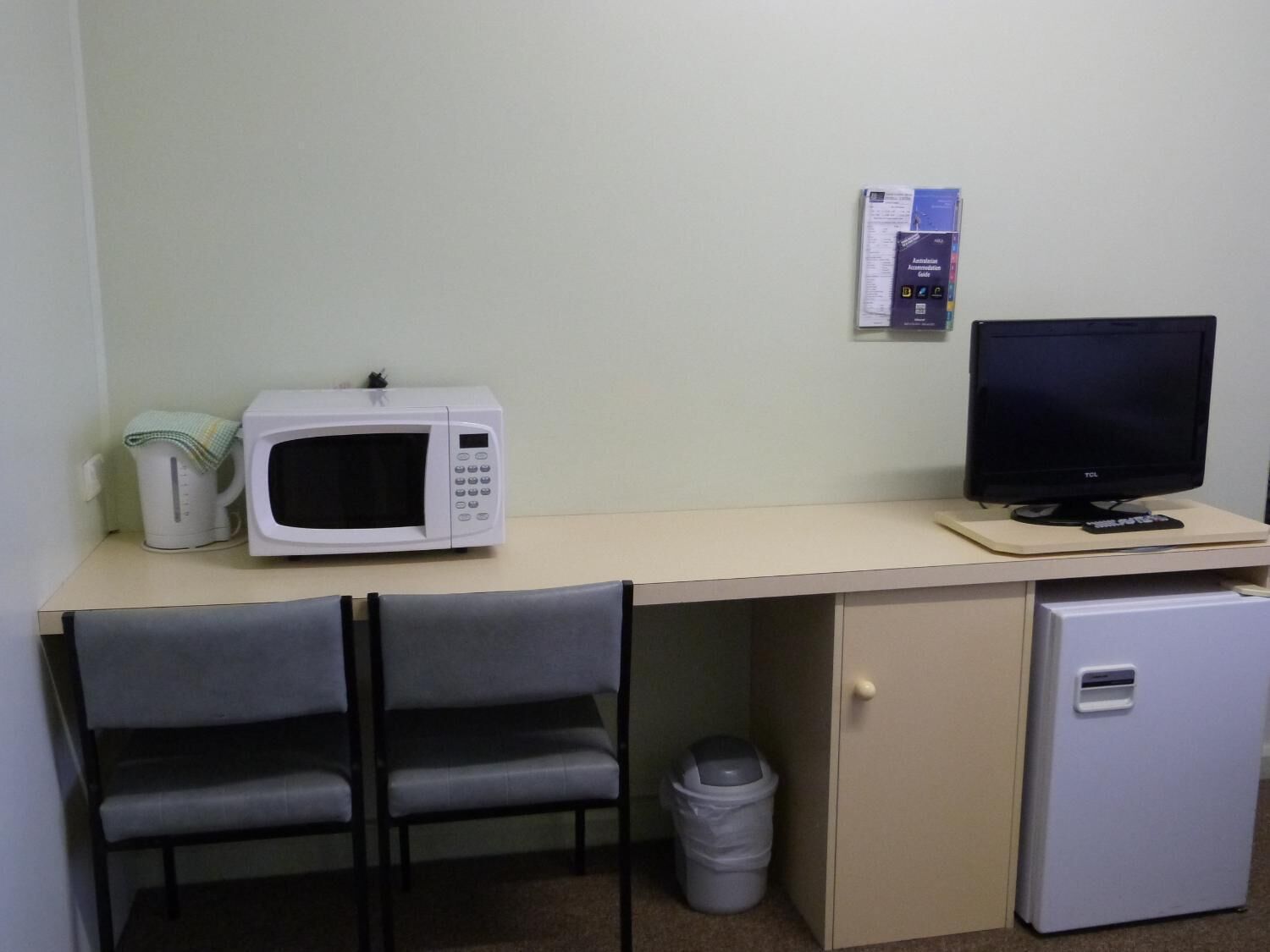 A small kitchenette with a microwave, a small refrigerator, a trash bin, and a chair.
