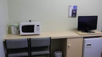 A small kitchenette with a microwave, a small refrigerator, a trash bin, and a chair.