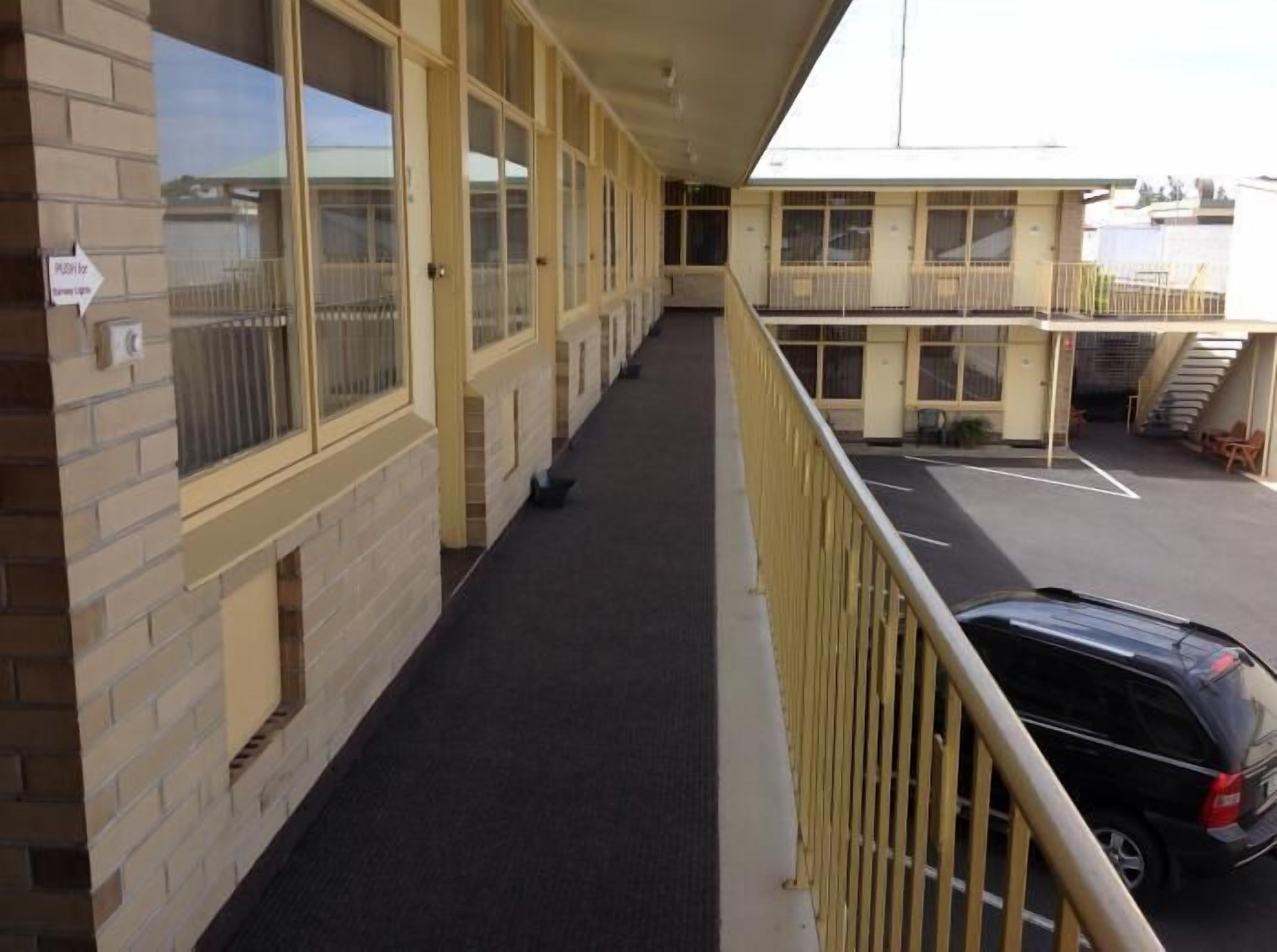 A long corridor with a black carpet, beige walls, and large windows.