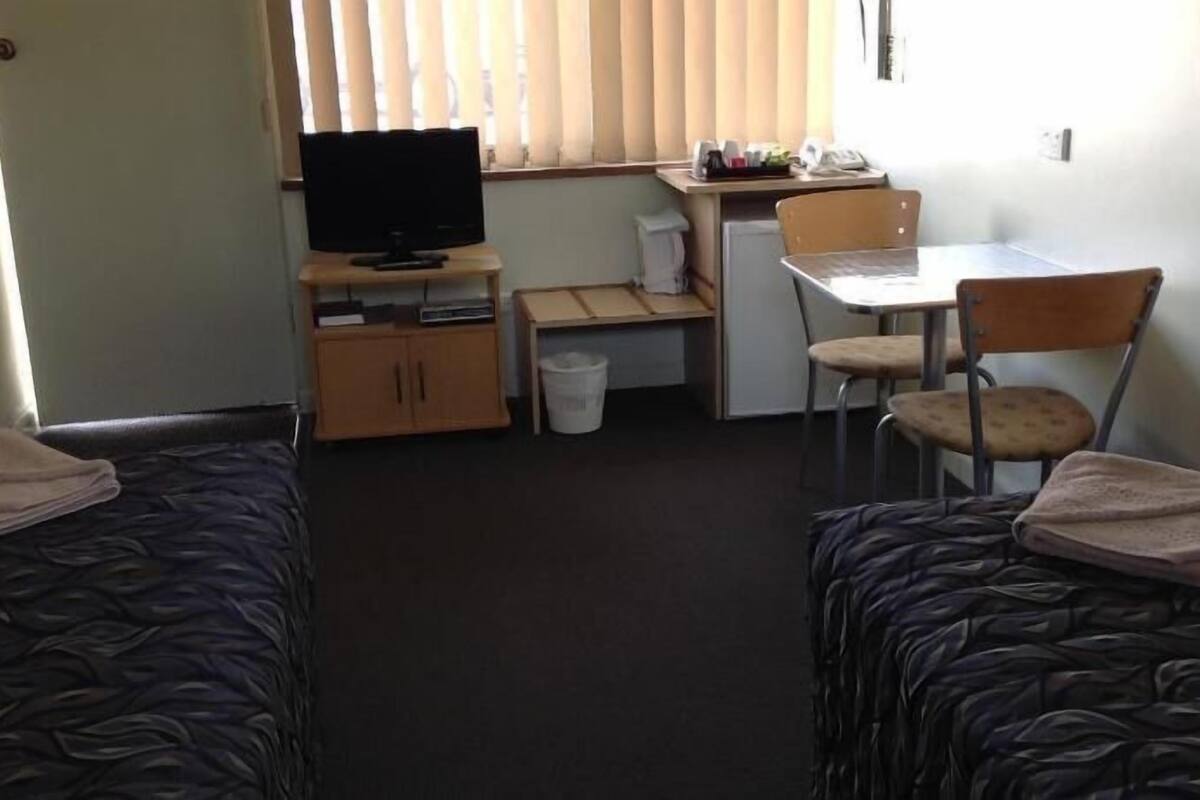 A room with two beds, a desk with a computer, a chair, and a television.