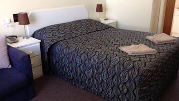 A hotel room with a patterned bedspread, a blue chair, two bedside tables with lamps, and a telephone on one of the tables.