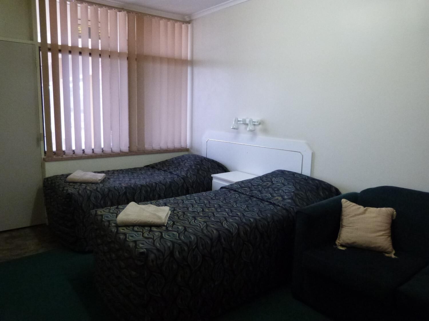 Ein kleines, schlichtes Zimmer mit zwei Einzelbetten, einem kleinen Tisch und einer Couch.
