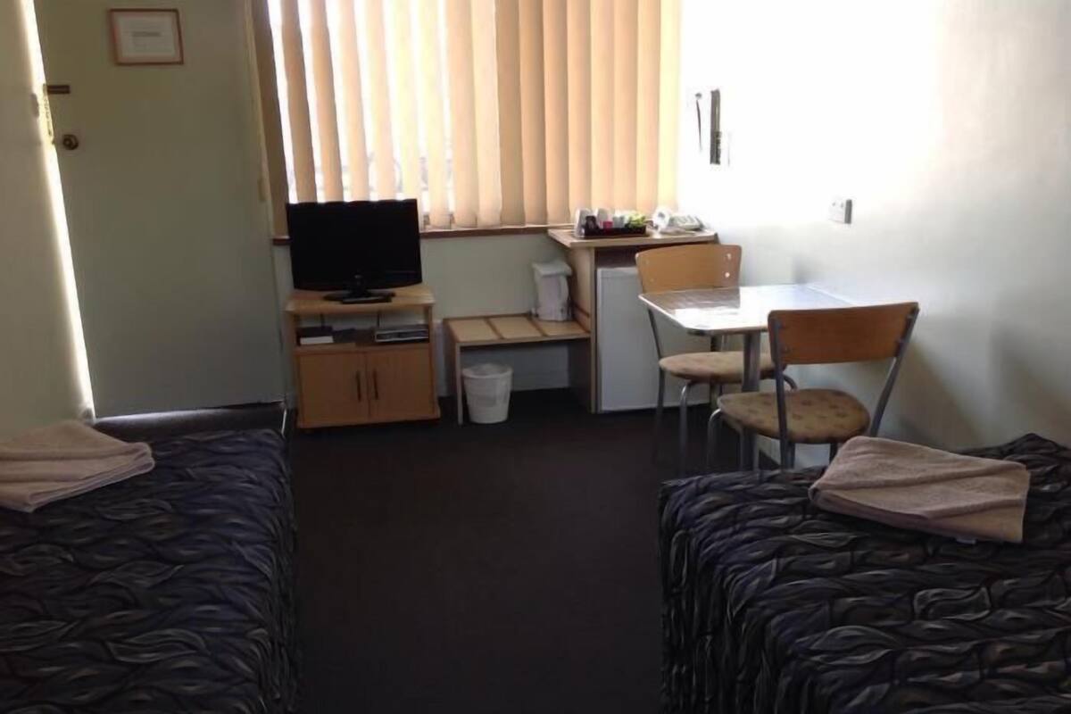 A room with two beds, a desk, a chair, a television, and a small kitchenette.