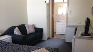 Habitación de hotel con cama, sofá, escritorio, kitchenette pequeña y televisor.