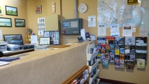 Mostrador de recepción con una computadora, un reloj y varios carteles informativos en la pared.