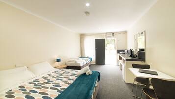 A hotel room with a bed, a desk, a chair, and a kitchenette.