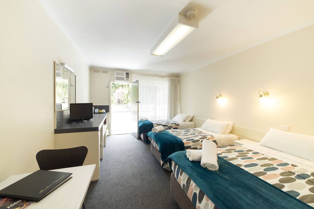 Habitación de hotel con dos camas, un escritorio con ordenador, una silla y una ventana con cortinas.