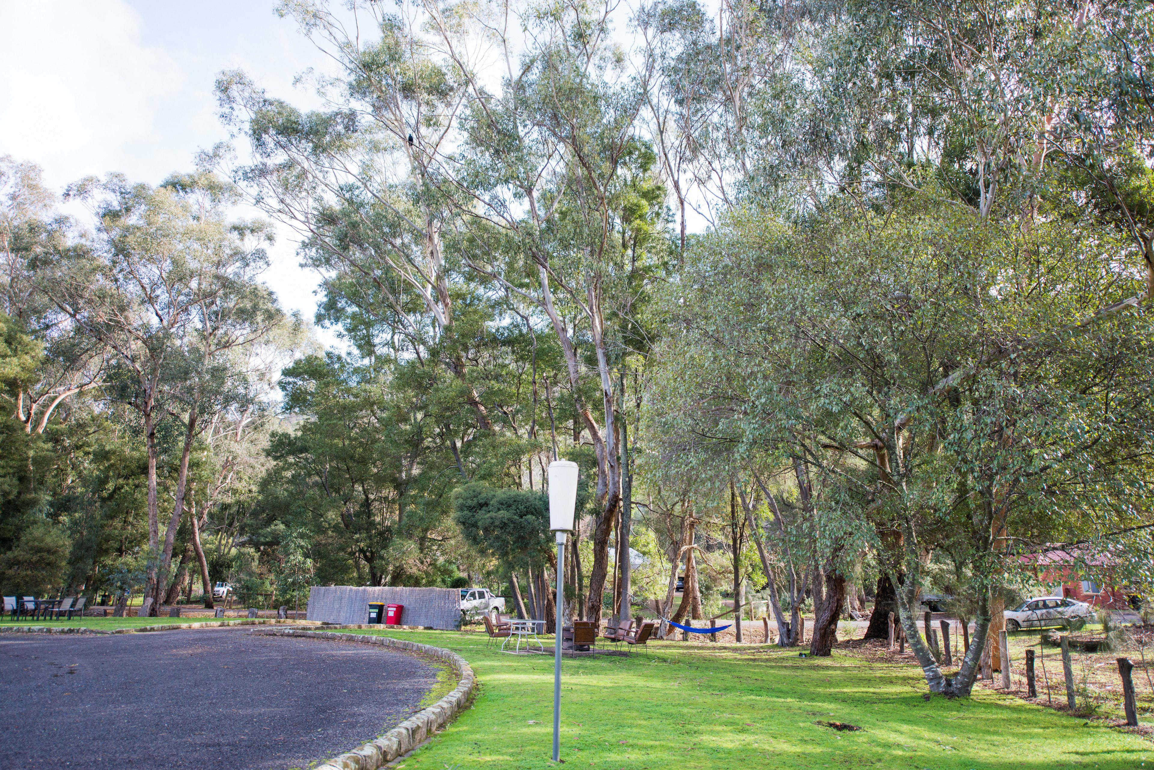 A park with a circular gravel area, trees, a small building, and a white vehicle in the background.