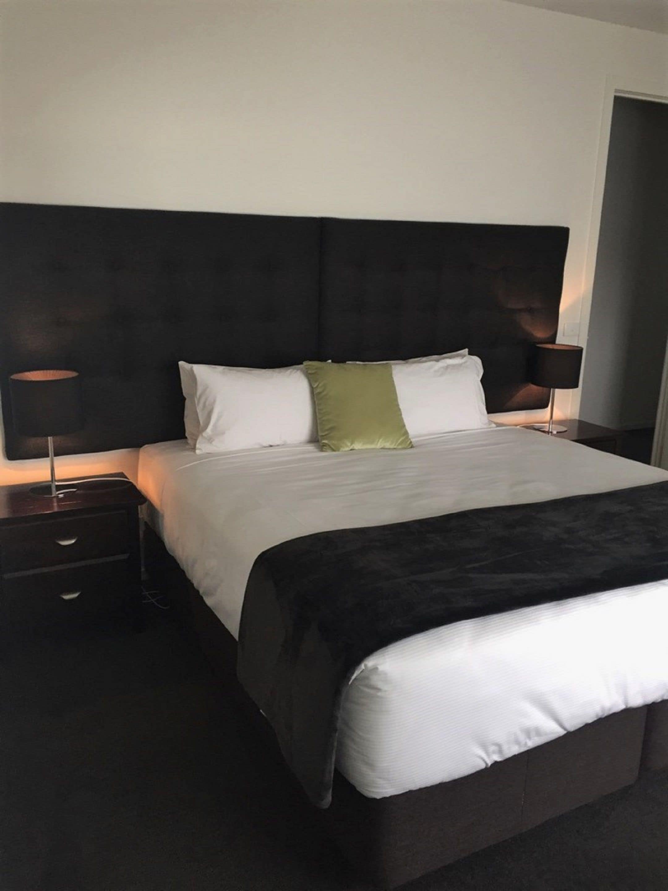 A hotel room with a large bed, two bedside tables, and a dark headboard.
