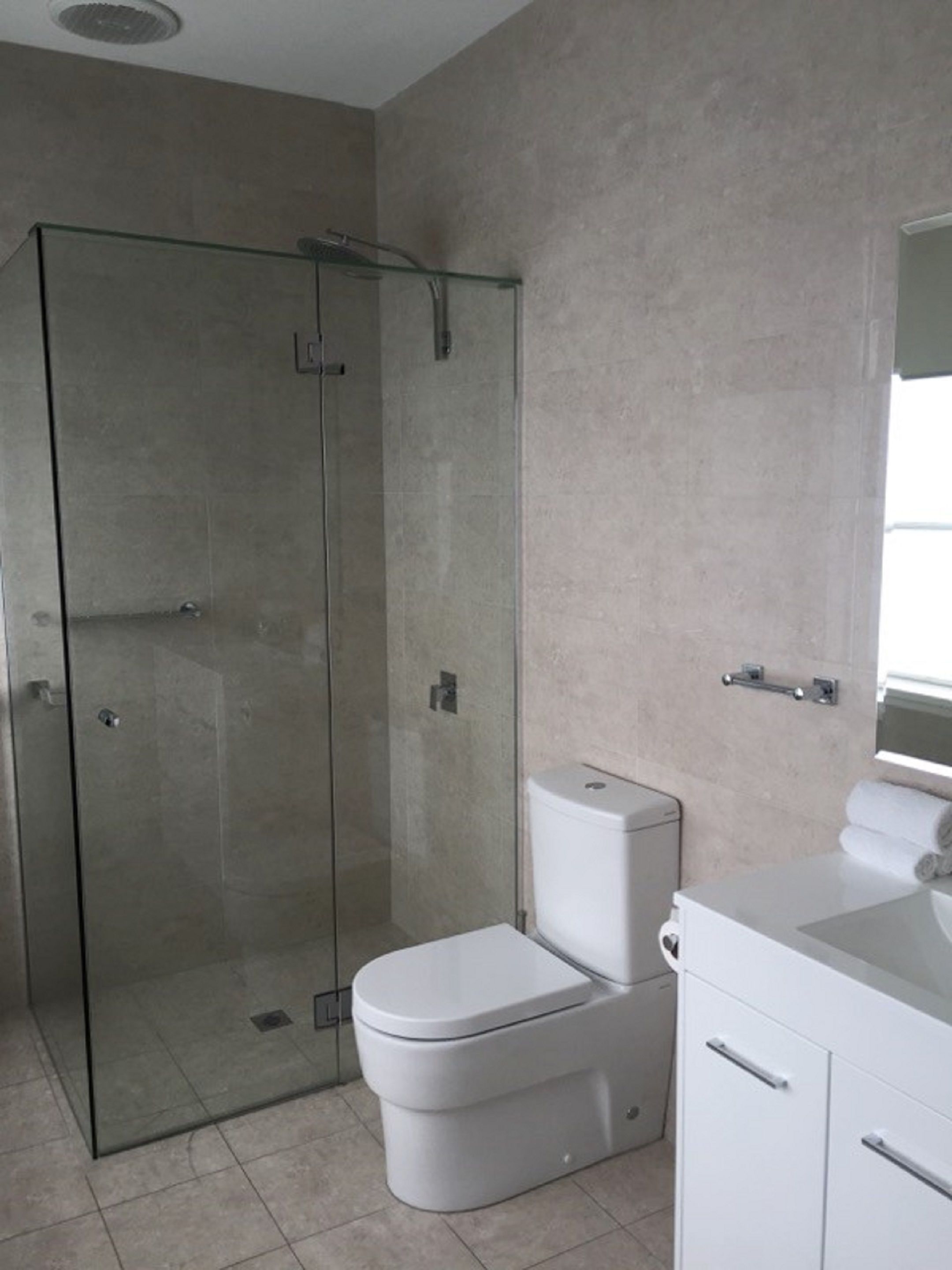 A modern bathroom with a glass-enclosed shower, a toilet, and a vanity with a mirror.