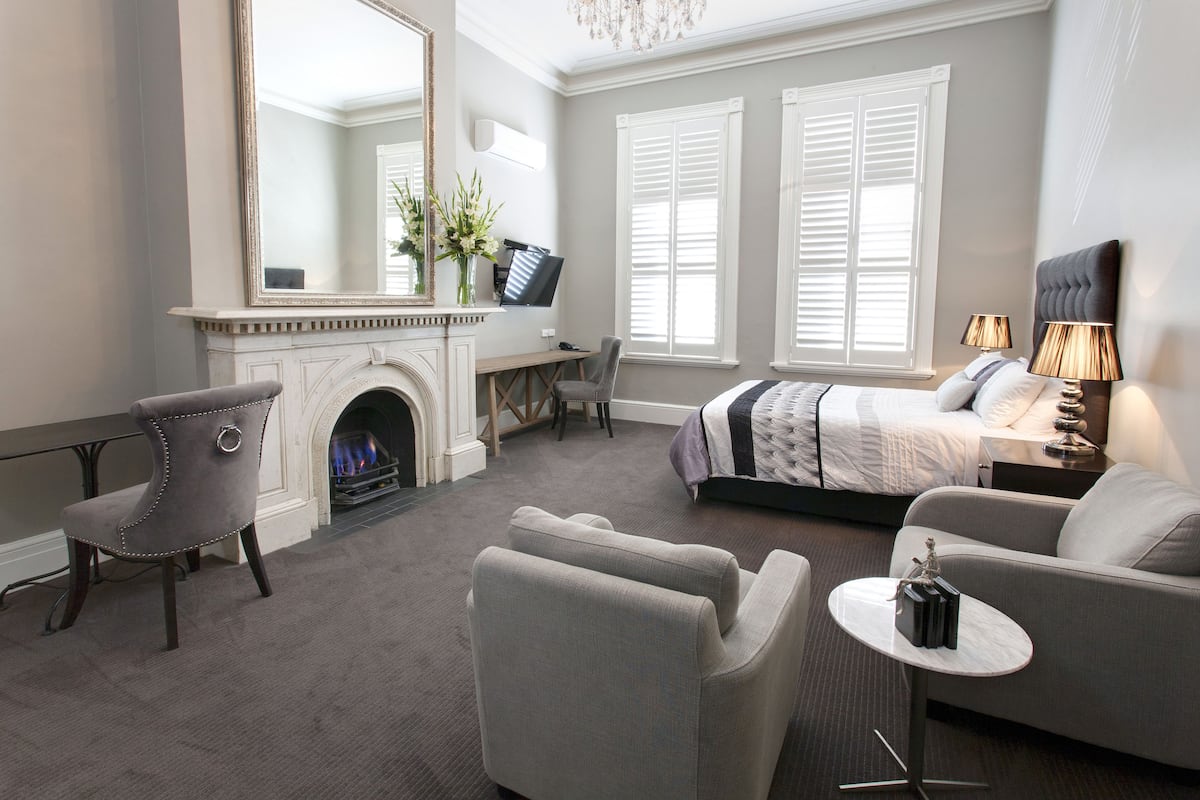 A modern hotel room with a fireplace, a bed, a sofa, a desk, and a TV.
