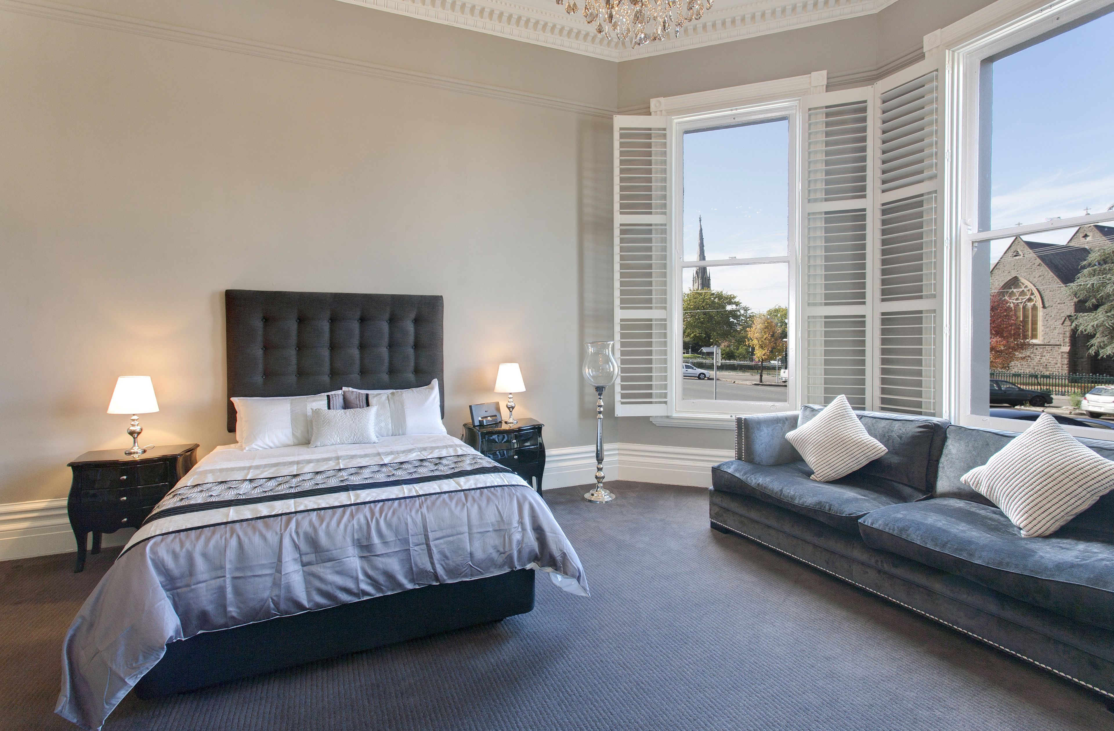 A bedroom with a large bed, a sofa, and a window with shutters.