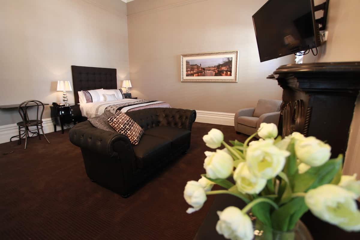 A bedroom with a bed, a sofa, a chair, a TV, and a fireplace.