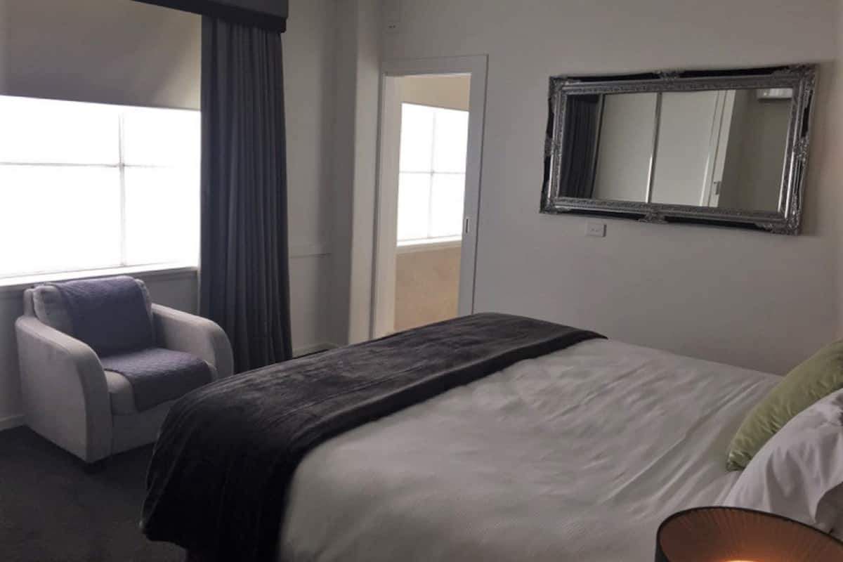 A hotel room with a bed, a chair, a large mirror, and a window.