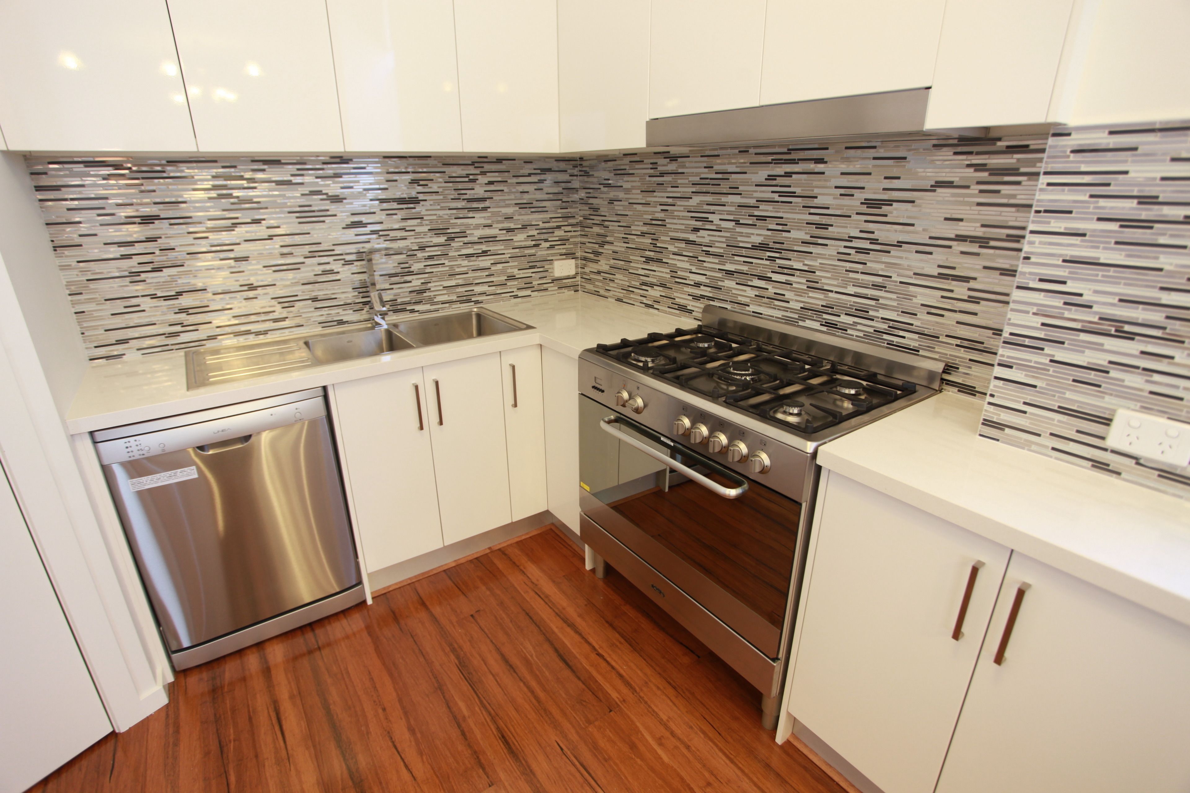 A modern kitchen with white cabinets, a stainless steel dishwasher, a gas stove, and a tiled backsplash.