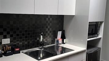 Una cocina moderna con armarios blancos, un salpicadero de azulejos negros, un lavamanos de acero inoxidable y un microondas integrado.