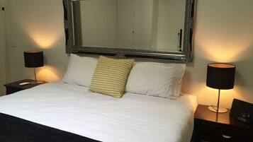 Ein ordentlich bezogenes Bett mit weißen Laken, ein großer Spiegel darüber und zwei Nachttische mit Lampen und einem Telefon.