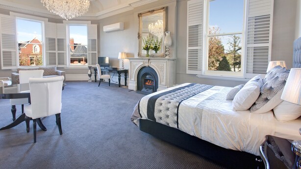Un dormitorio con una cama grande, un escritorio, una silla, una chimenea y ventanas amplias.