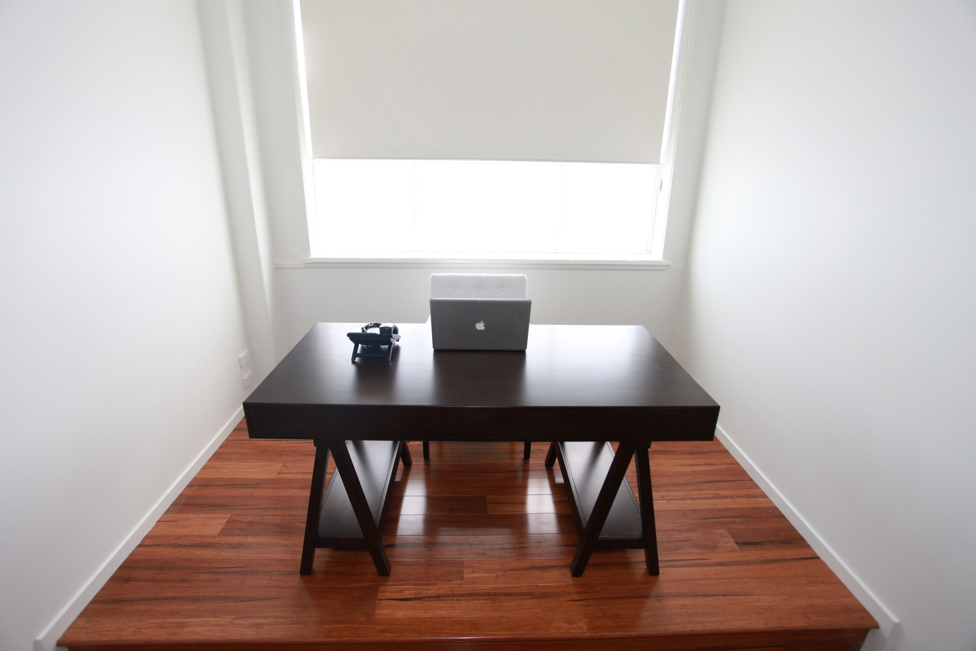 A room with a dark wooden table, a laptop, and a small electronic device on it.