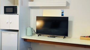 A room with a television on a stand, a microwave above a cabinet, and a kettle on the counter. - Stonez Boutique Accommodation (Clunes)