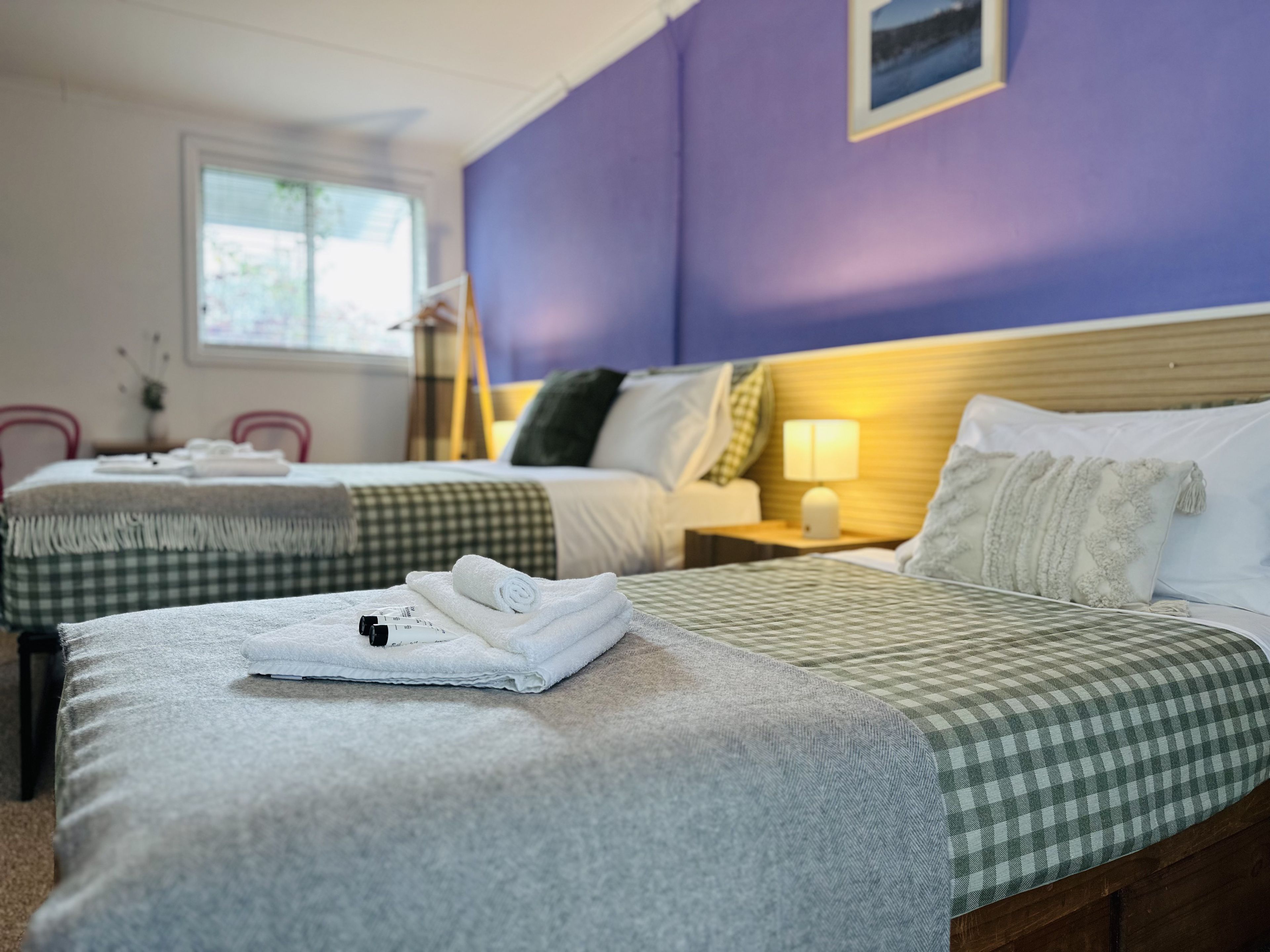 Une chambre d’hôtel avec deux lits, des couvre-lits à carreaux, une table de chevet avec une lampe et une fenêtre donnant sur un paysage agréable.