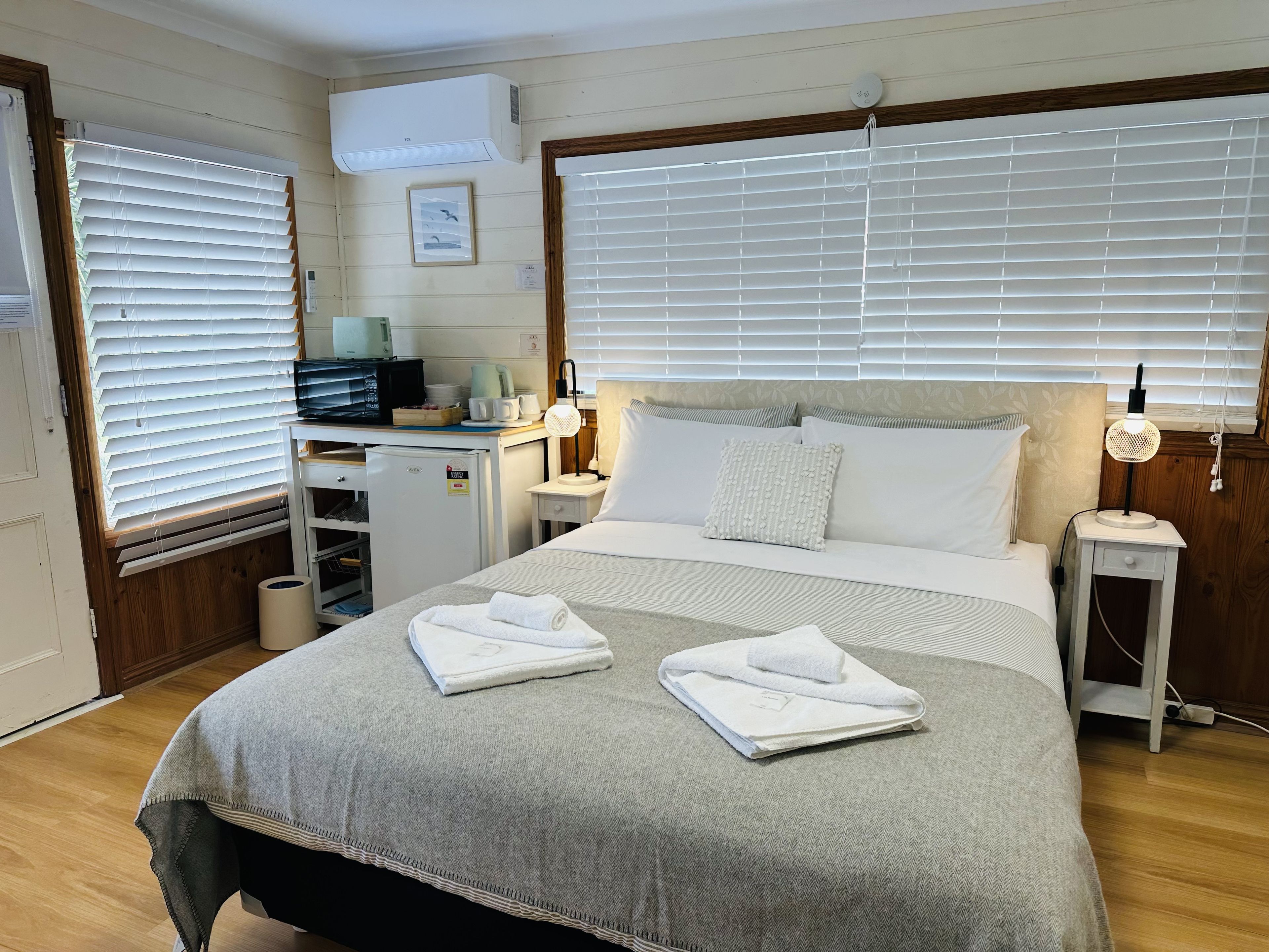 Une chambre d’hôtel équipée d’un lit, de tables de chevet, d’un bureau et d’une fenêtre avec des stores.