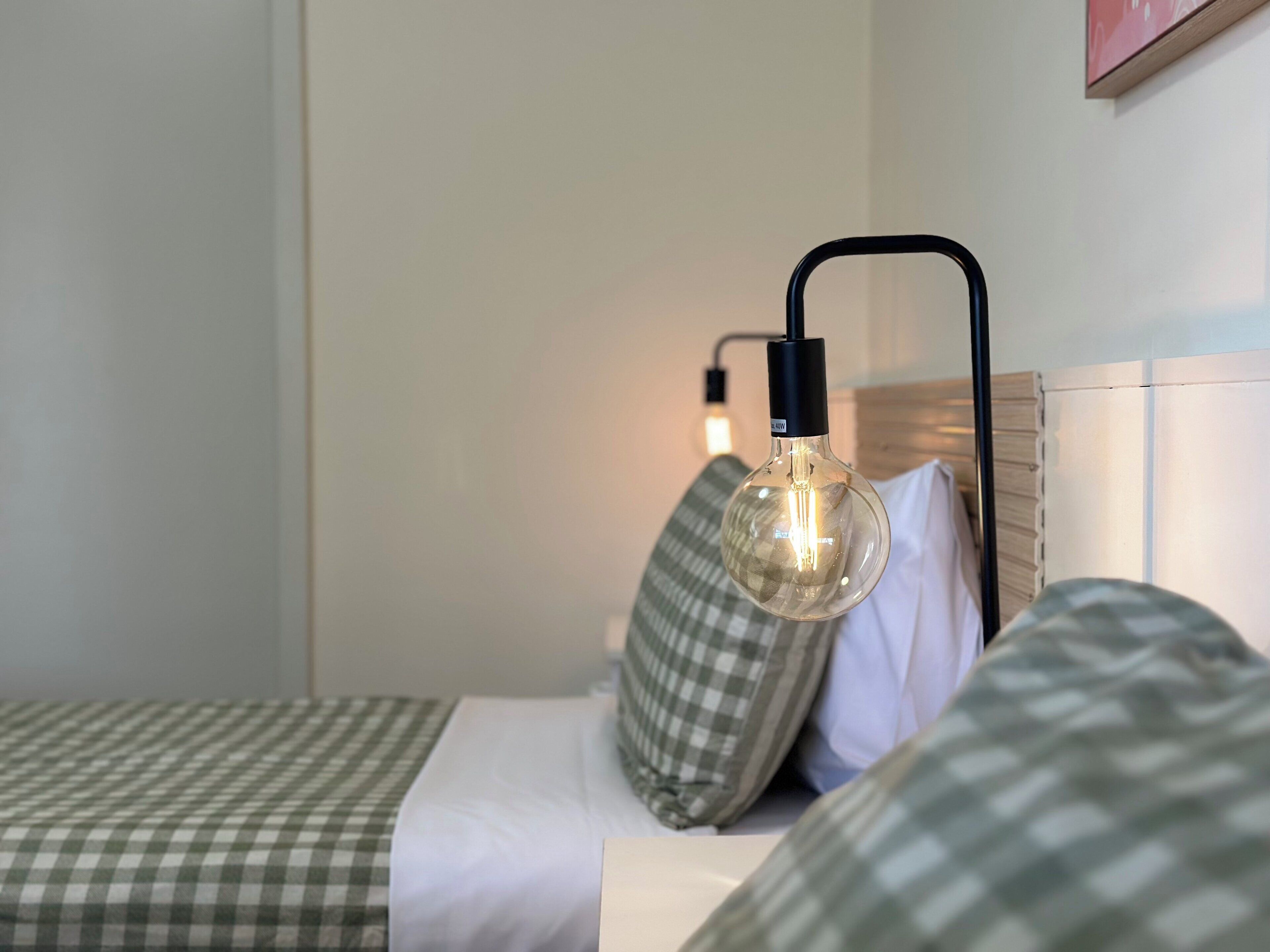 Ein Bett mit kariertem Überwurf, einem Kopfkissen und einer Hängelampe.