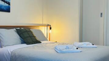 A hotel room with a bed, pillows, a nightstand, a lamp, and a painting on the wall.