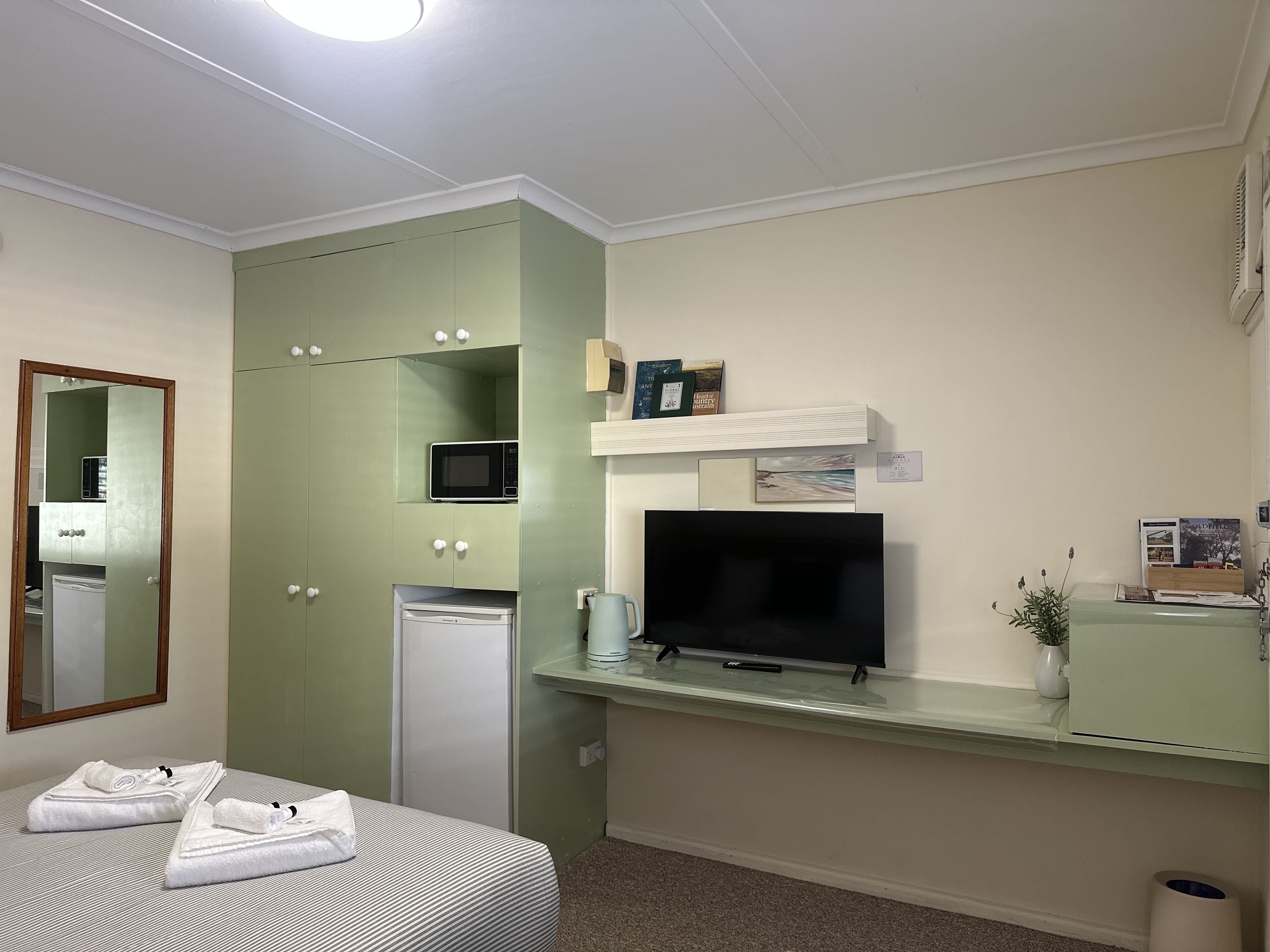 Habitación de hotel con cama, televisor, microondas, refrigerador pequeño y un mueble con espejo.