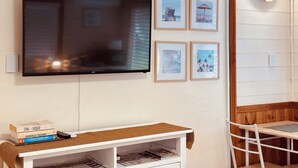 A flat-screen TV mounted on a wall, a small white table with a woven table runner, and a white chair. - Stonez Boutique Accommodation (Clunes)