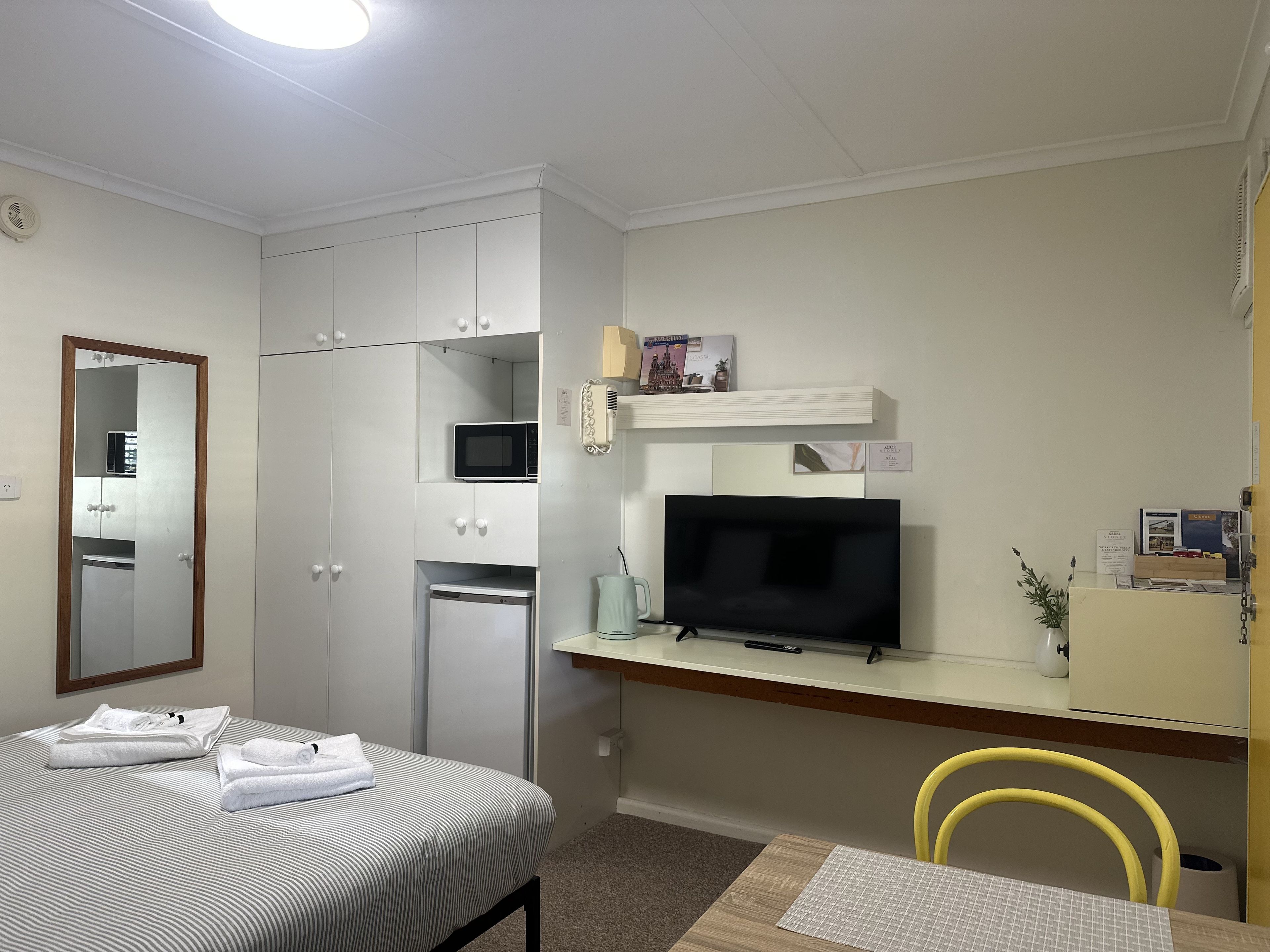 Una habitación de hotel con una cama, un escritorio con televisor, microondas y un refrigerador pequeño.