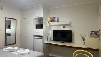 Una habitación de hotel con una cama, un escritorio con televisor, microondas y un refrigerador pequeño.