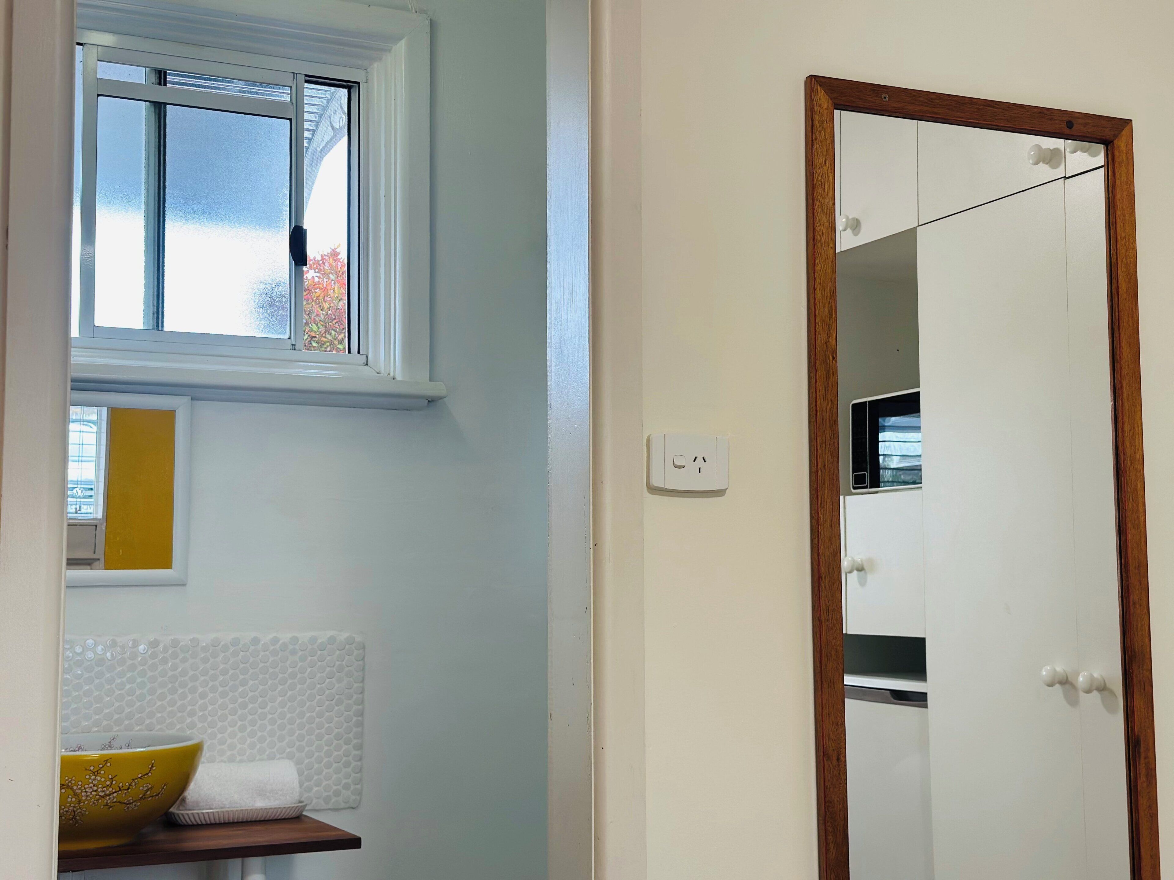 Una habitación con ventana, espejo, pared blanca y puerta.