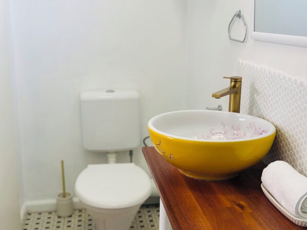 A bathroom with a toilet, a yellow sink with floral design, and a towel on the counter.