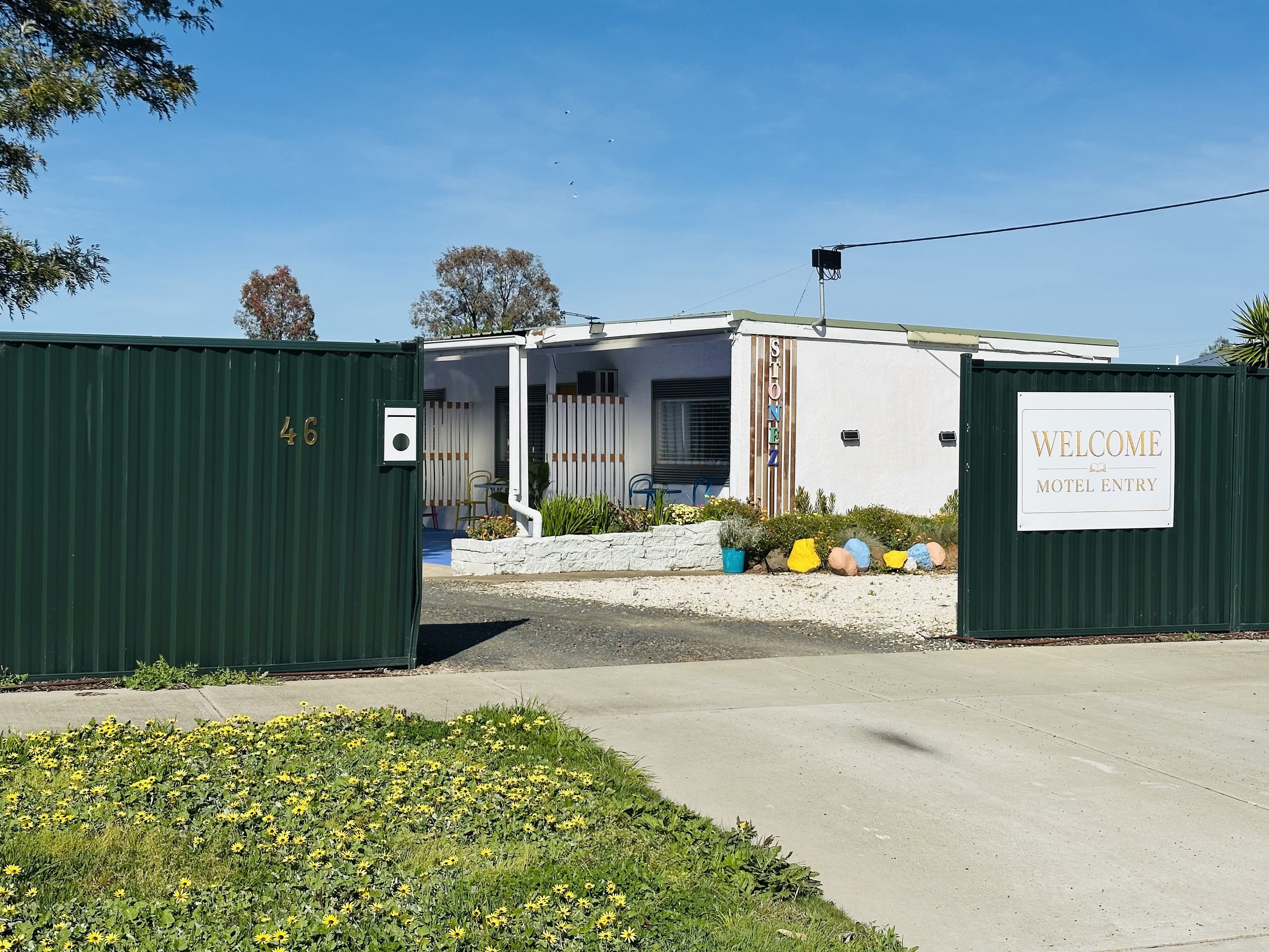 De ingang van een motel met een 'Welcome'-bord, een hek en een gebouw met een witte gevel.