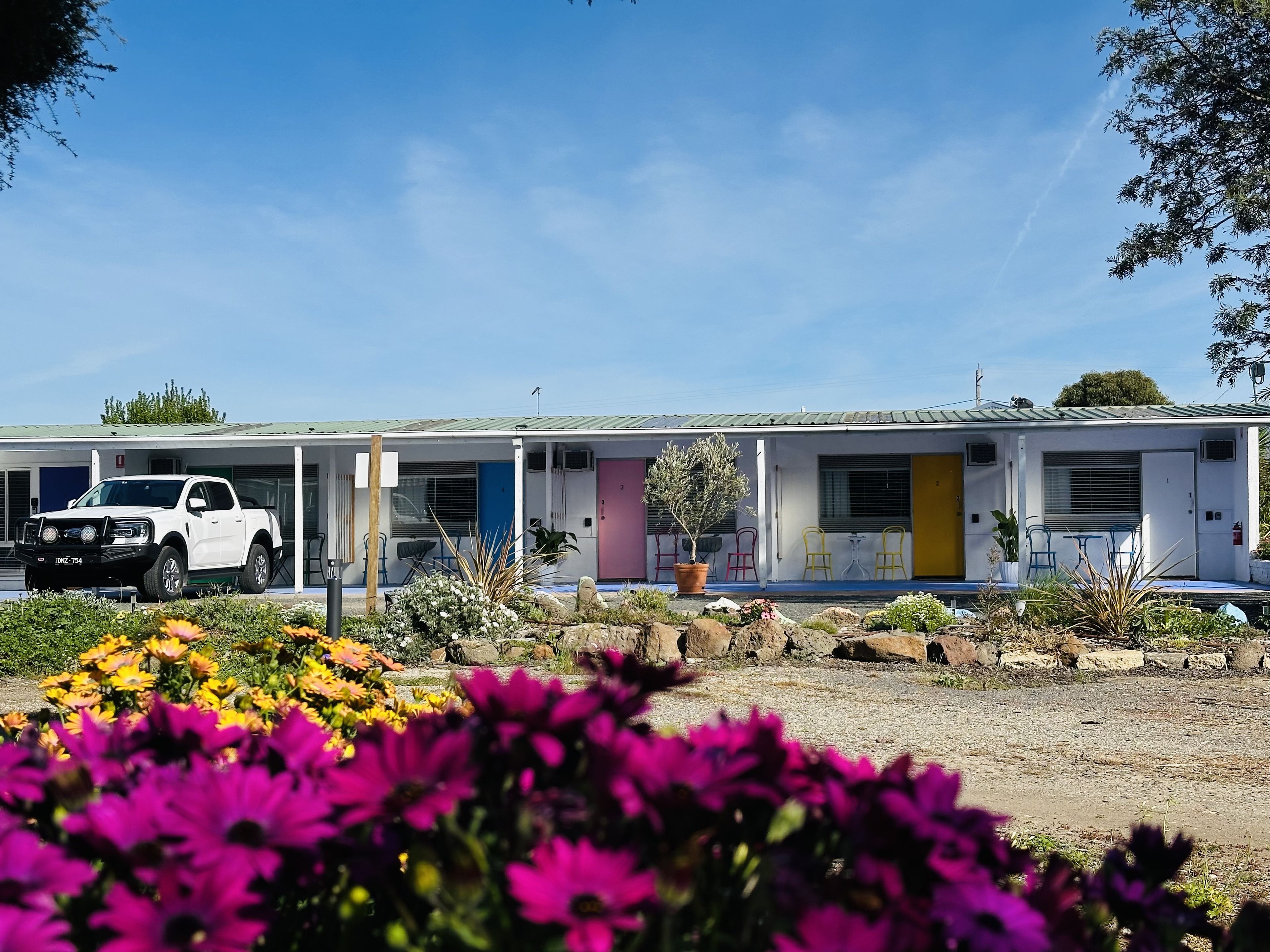 Un motel à l’extérieur blanc, avec de nombreuses portes et un véhicule garé devant.