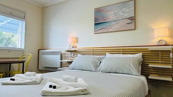 A hotel room with a bed, a painting, a desk, and a chair.