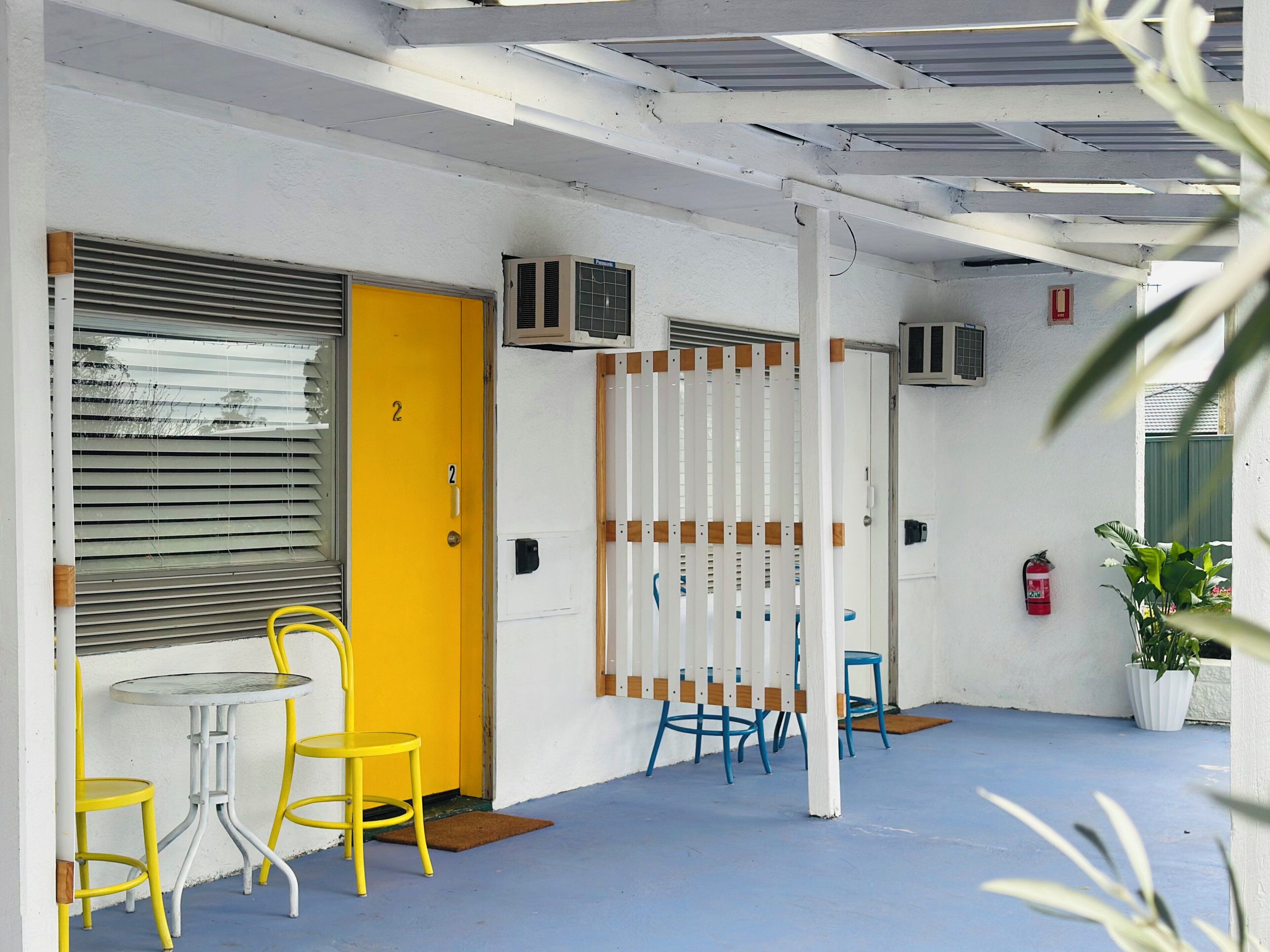 A room with a yellow door, a white wall, a blue floor, and a table with yellow chairs.