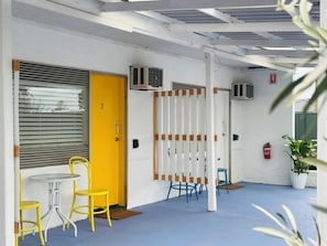 Una habitación con puerta amarilla, pared blanca, piso azul y una mesa con sillas amarillas.
