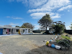 Un motel con una zona de estar al aire libre techada, un árbol grande y un estacionamiento de grava.