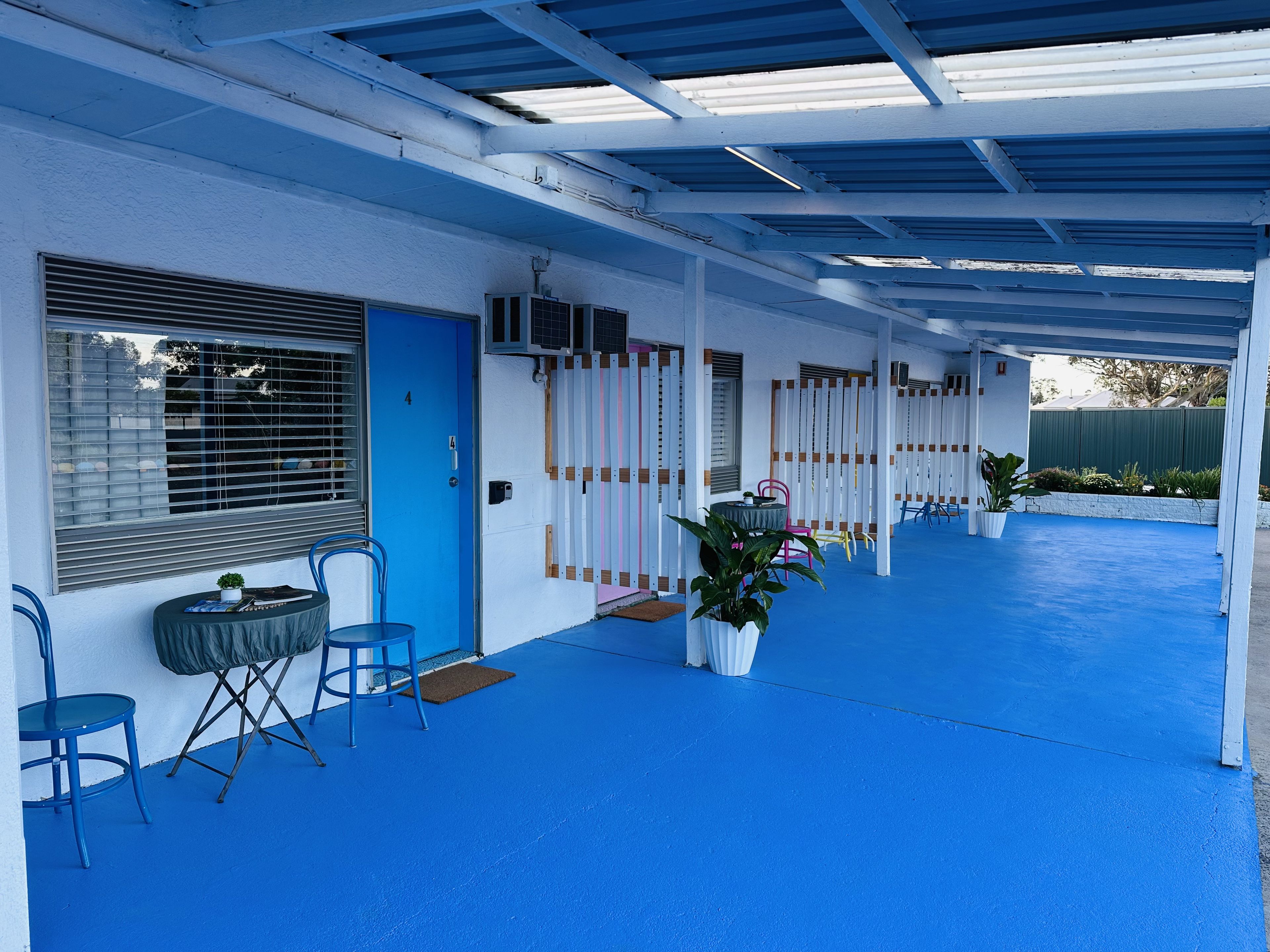 A covered outdoor area with a blue floor, a blue door, and a window with blinds.