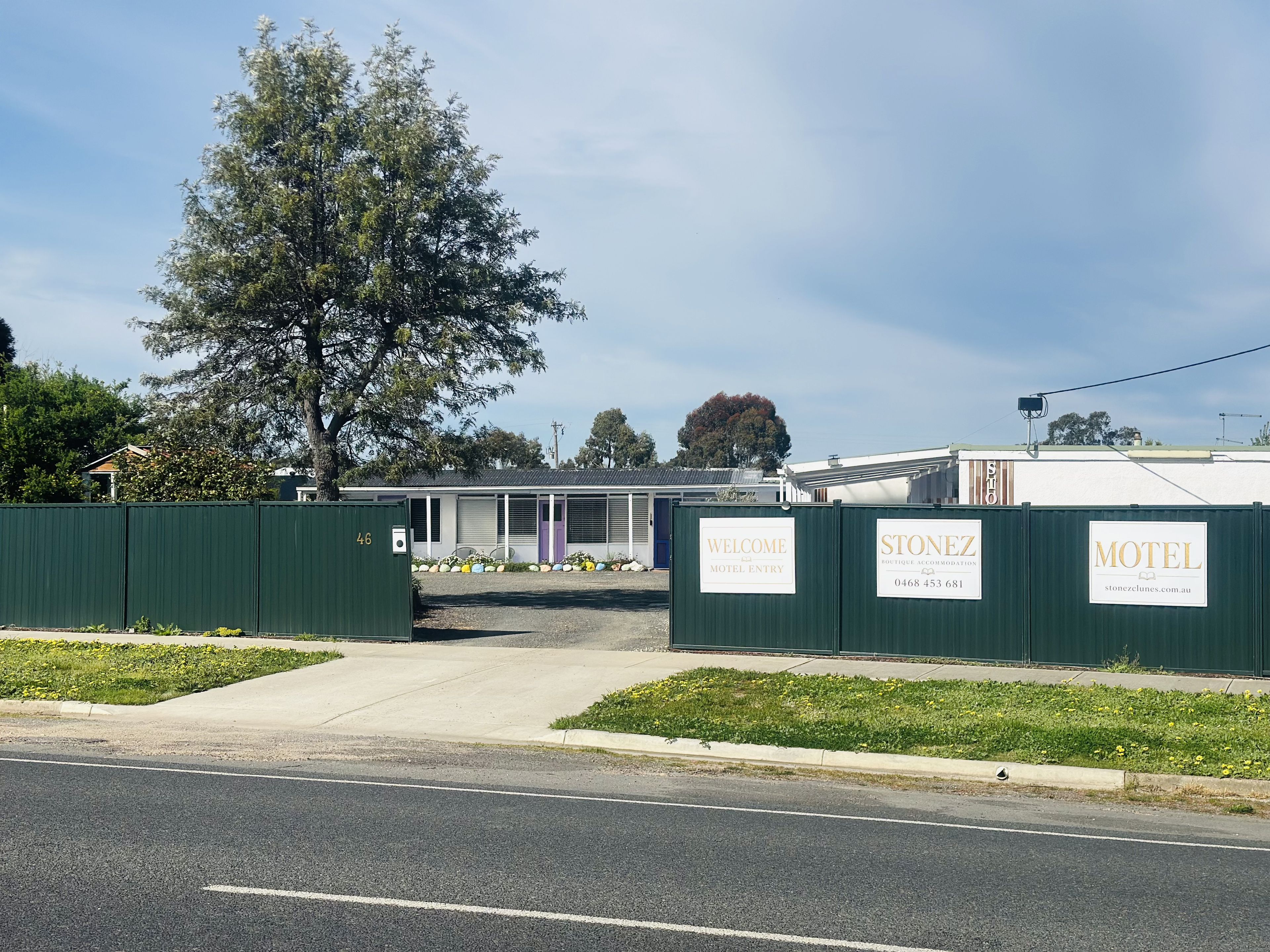 A motel with a green fence, a welcome sign, and a stonez boutique accommodation sign.