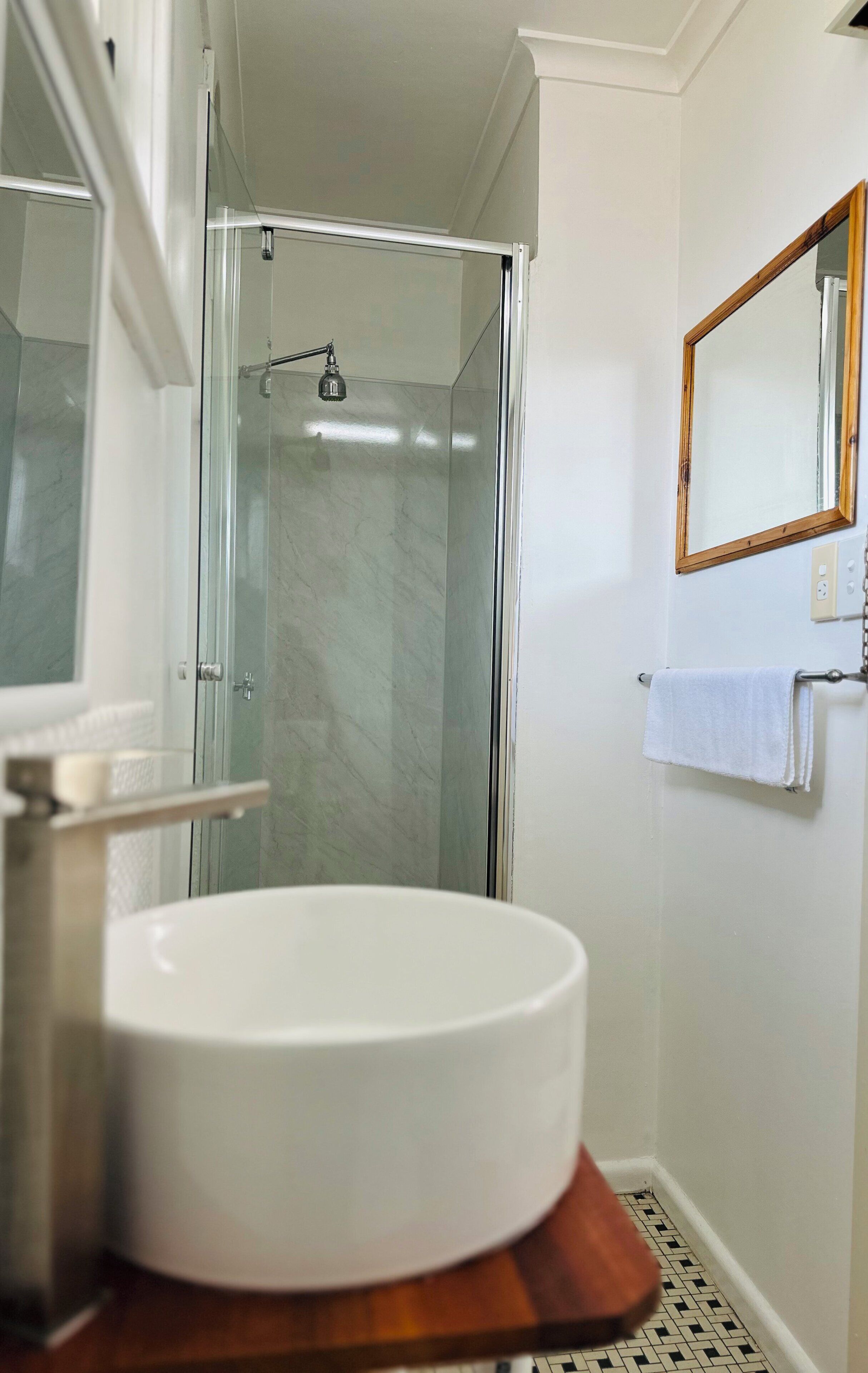 Een badkamer met een douche in een glazen cabine, een wit wastafeltje en een houten meubel.
