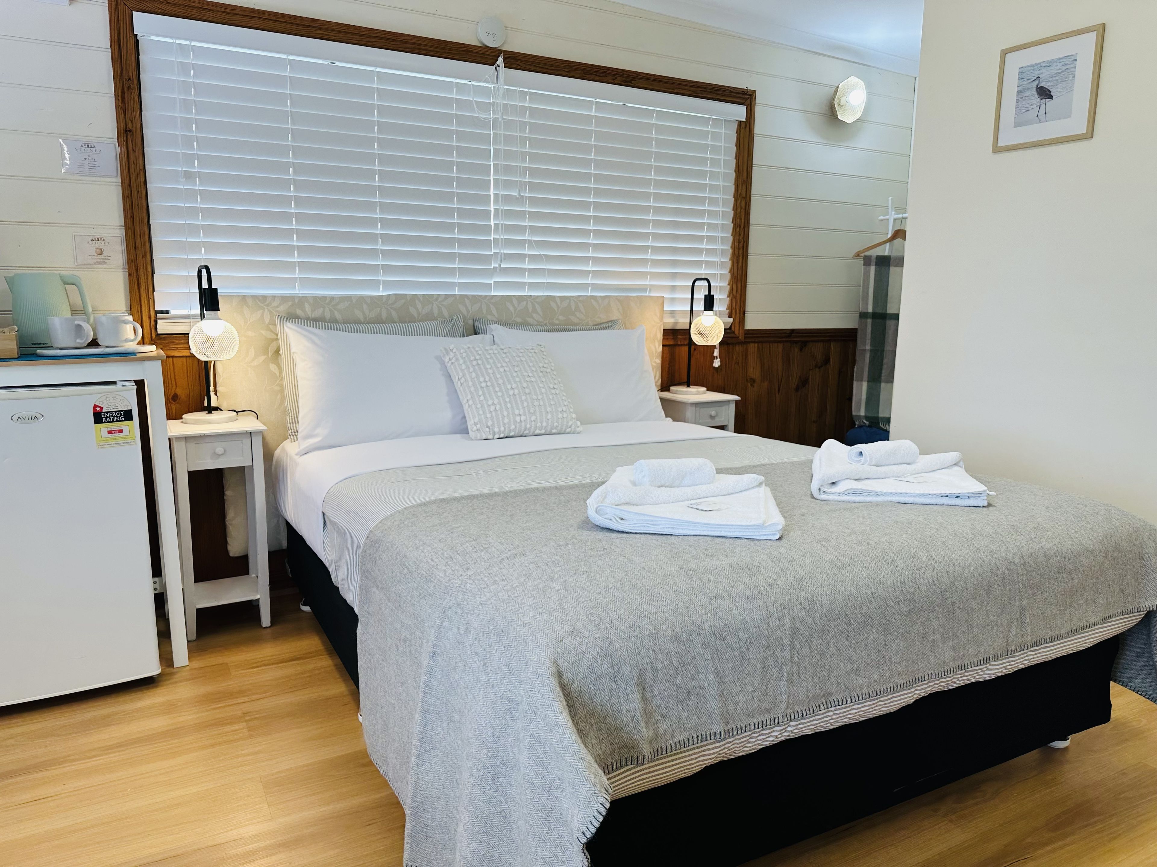 Une chambre d’hôtel avec un lit, des tables de chevet, un bureau et une fenêtre avec des stores.