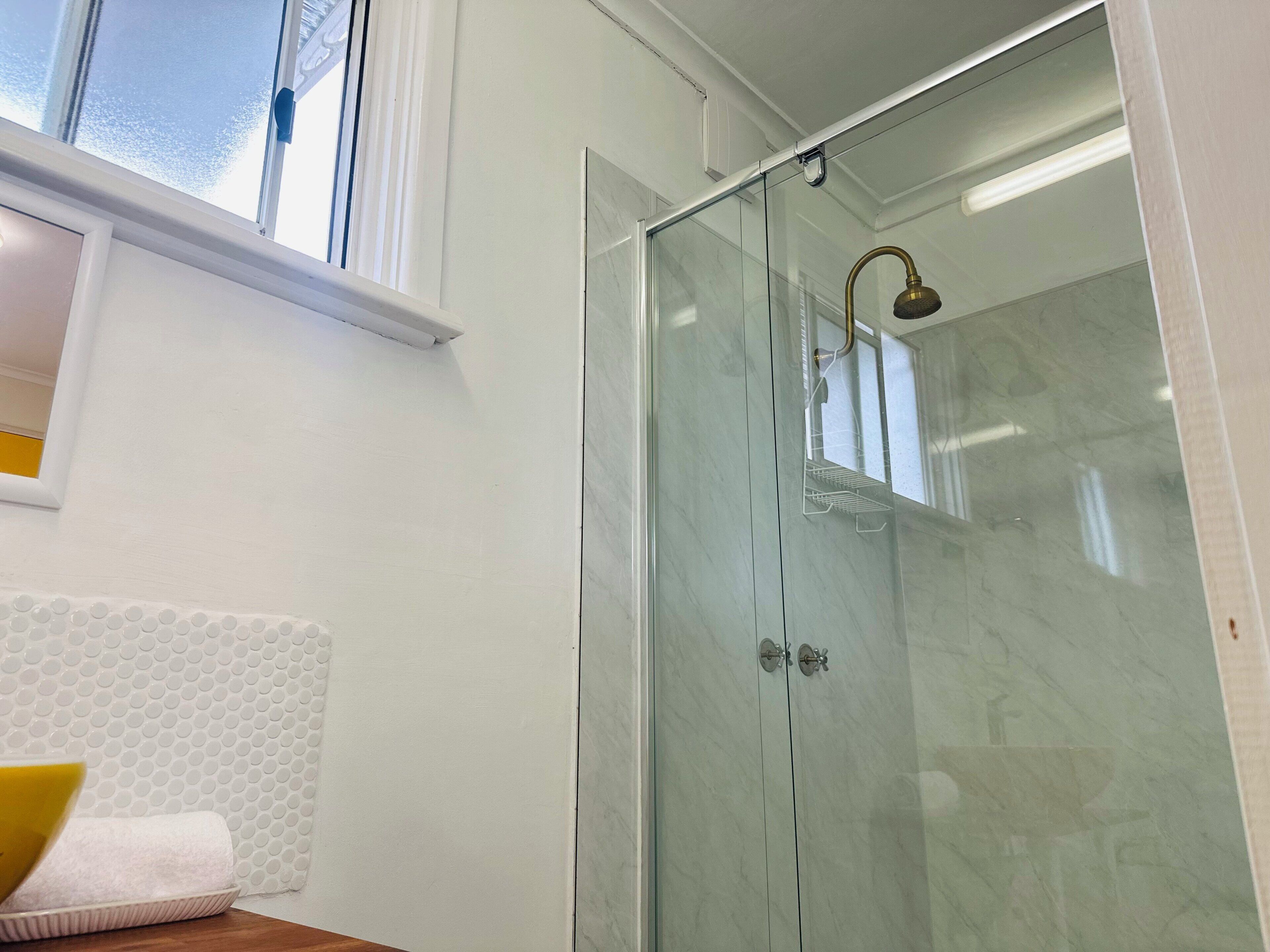 A bathroom with a glass shower enclosure, a white bathtub, and a window above the shower.