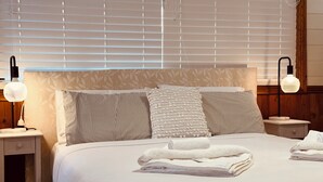 A neatly made bed with pillows and folded towels, a bedside table with a lamp, and a window with blinds. - Stonez Boutique Accommodation (Clunes)