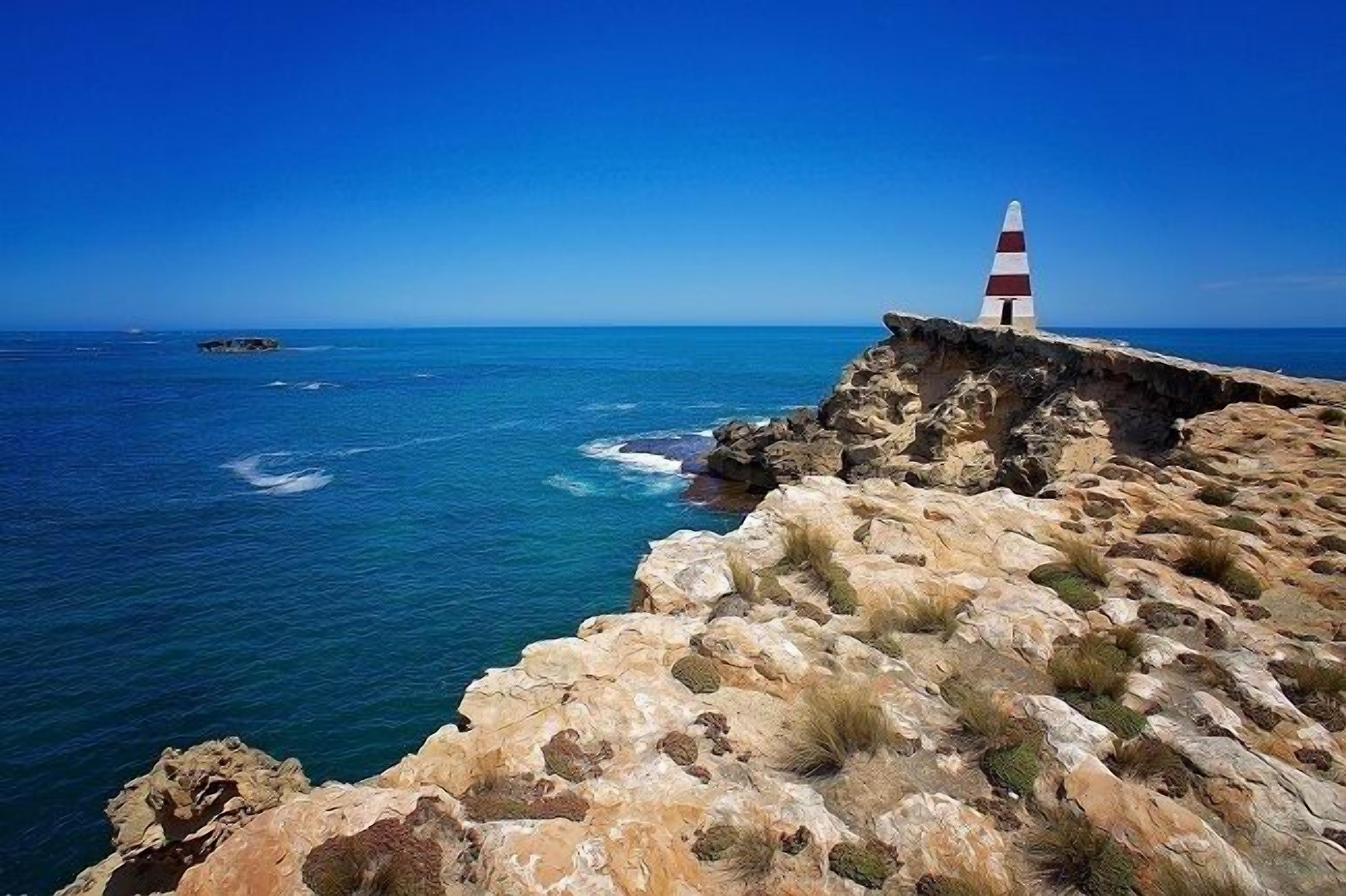 Un paysage côtier avec un phare situé sur un promontoire rocheux.