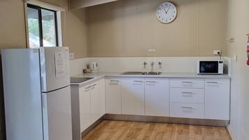 A kitchen with white cabinets, a microwave, a refrigerator, a sink, and a clock on the wall.